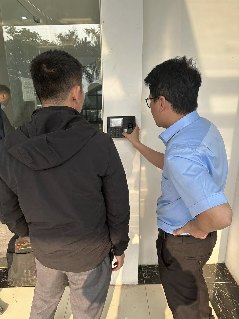 Hai người kiểm tra danh s&aacute;ch nh&acirc;n vi&ecirc;n tr&ecirc;n m&aacute;y chấm c&ocirc;ng