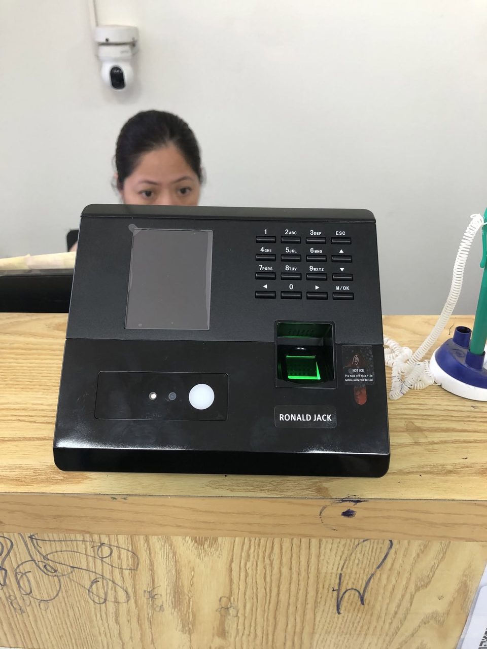 Nh&acirc;n vi&ecirc;n đứng sau m&aacute;y chấm c&ocirc;ng khu&ocirc;n mặt đặt tr&ecirc;n b&agrave;n